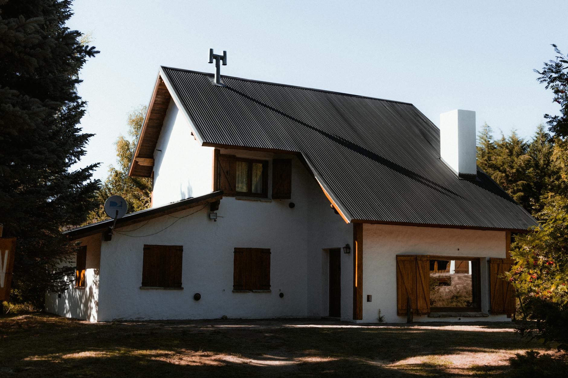 A rustic country house with wooden shutters surrounded by lush greenery under daylight.