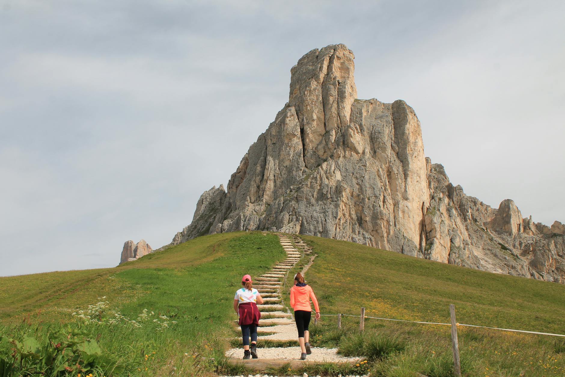 Two women hiking towards the majestic Passo Giau in Veneto, Italy, showcasing stunning natural landscapes.